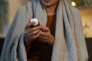 Medication Management. Woman holding medicine bottle while wrapped in blanket.
