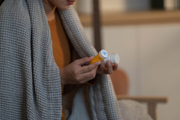Health and Wellness. Woman holding medication bottle, wrapped in cozy blanket.