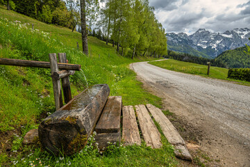 Mountain road with wooden water trough and alpine view
