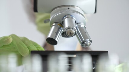 Close up of green gloved hands of a scientist adjusting a microscope in a laboratory, emphasizing the significance of scientific research and analysis. Medicine, healthcare and science concept