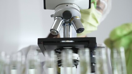 Scientist in green protective mask and gloves holding test tube with plant sample, researching...
