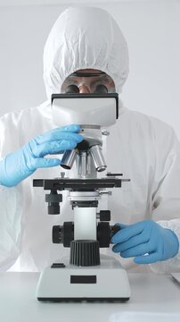 Medical virologist in protective hazmat gear examining viral samples under a microscope while conducting research in a sterile laboratory environment