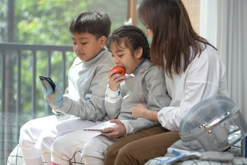 The fencer relaxes by spending time on his cell phone and eating an apple while his mother looks after them. Caring for growing children