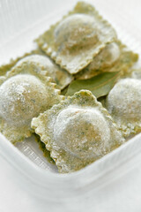 A Close-Up View of Freshly Made Green Ravioli Tucked in a Container with Aromatic Bay Leaves and a Light Dusting of Flour