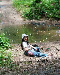 Lifestyle, Asian Woman travel on vacation. Ecotourism adventure, explore nature butterfly in forest. She is sitting riverside relax happy, among colorful butterflies flying. Kaeng Krachan, Thailand.