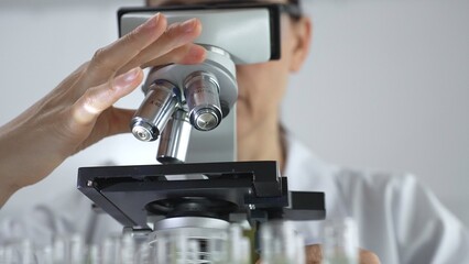 Female scientist analyzing test samples under microscope in contemporary research environment of laboratory. Medicine, healthcare and science concept