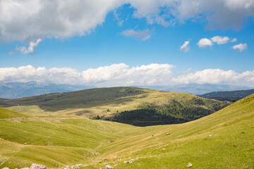 Landscape of green meadows between mountains, with a blue sky with clouds.
