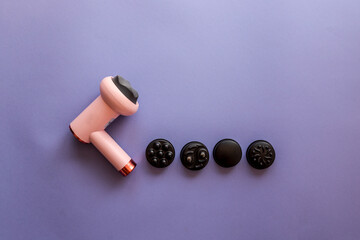 Pink massage gun with five black interchangeable heads arranged on purple background. Modern...