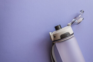 Reusable sports water bottle with flip-top lid and carrying strap on a purple background....
