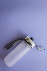 Minimalist sports water bottle with carrying strap and flip-top lid on a light purple background....
