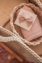 Soft pink baby headband with bow on a white card, placed on a muslin cloth inside a knitted baby...