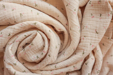 Close-up of soft beige muslin fabric with tiny floral print, artistically rolled into a spiral....