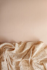 Crinkled beige muslin fabric with tiny floral print, softly draped on a neutral background. Light,...