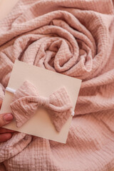 Close-up of a handmade pink baby headband with a soft cotton bow, displayed on a card against...