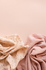 Two soft muslin fabrics in pastel pink and cream with floral patterns arranged on a minimal beige...