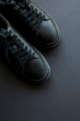 Pair of black leather sneakers with laces placed on a dark monochrome background. Minimalist...