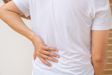 Asian man suffering back pain from household chores, illustrating muscle strain or injury. Ideal...