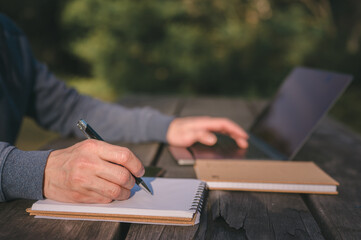 Outdoor Study or Journaling Concept, Close-Up of Man Writing in Notebook in Natural Park...