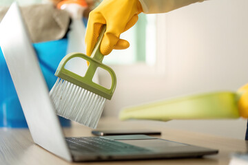 Home Cleaning. Woman using brush to clean laptop with yellow rubber gloves.