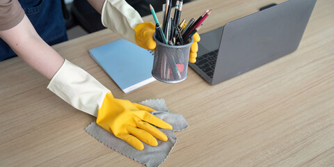 Home Cleaning. Woman organizing her workspace while cleaning the desk with yellow gloves.