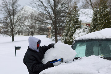 A portrait of a black man cleaning snow off of a windshield in the winter after a blizzard 