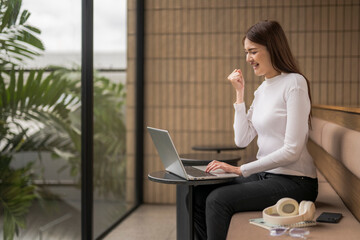 Excited young businesswoman celebrating success while working on laptop in modern office
