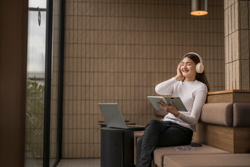 Young asian freelancer woman listening music and reading book in coworking space