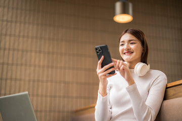 Smiling freelancer using smartphone in modern cafe with laptop and headphones
