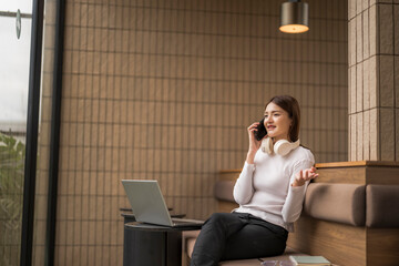 Young freelancer talking on phone while working on laptop in modern coworking space