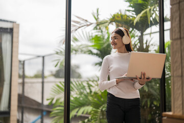 Young woman working remotely using laptop and headphones near window