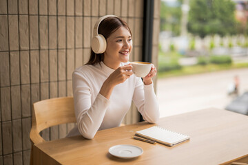 Young woman listening music with headphones and drinking coffee in cafe