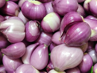 A pile of bright purple fresh shallots with some of the skin peeled off, revealing their natural...
