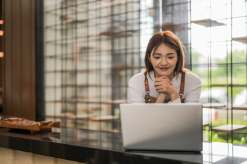 Smiling barista managing orders on laptop in coffee shop