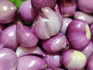 A pile of bright purple fresh shallots with some of the skin peeled off, revealing their natural...