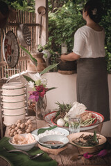 Mother is making chili paste and placing food on the table, along with rice, stir-fried morning glory, and omelet. Retro Thai style photo.