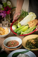 Mother holds a tray of fresh vegetables, places food on the table, shrimp paste chili paste,...
