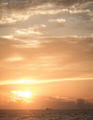 Obraz premium Tranquil sunset over the ocean with soft orange clouds and a boat silhouetted in the distance. Peaceful scene capturing serenity, isolation, and the power of nature.