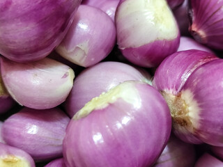 A pile of bright purple fresh shallots with some of the skin peeled off, revealing their natural...
