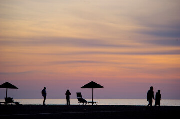 silhouette of a man walking on the beach at sunset, Silhouettes of umbrellas and people on the beach at Piscinas Ingurtosu. Arbus, Medio Campidano, Sardinia, Italy