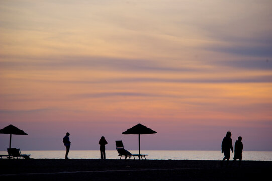 silhouette of a man walking on the beach at sunset, Silhouettes of umbrellas and people on the beach at Piscinas Ingurtosu. Arbus, Medio Campidano, Sardinia, Italy