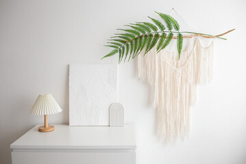 Table lamp with a white corrugated shade and white trendy decor stand on chest of drawers. Macrame...