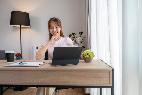 Young asian businesswoman working from home using tablet and smiling