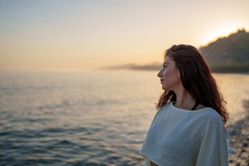 Side view portrait of a young woman admiring a beautiful sunset over the sea, feeling a sense of...