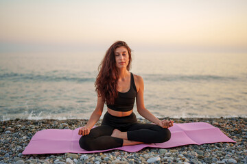 Yoga instructor performing meditation on a pebble beach at sunset, promoting wellness and...
