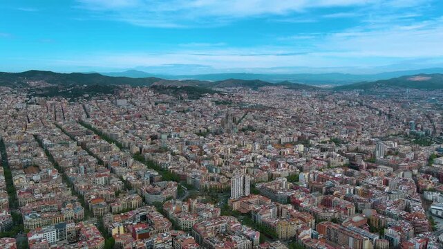 Wide aerial of Barcelona: Sagrada Fam&iacute;lia rises inside the razor‑straight Eixample grid, backed by green hills and bright Mediterranean light&mdash;ideal for travel and urban stories.