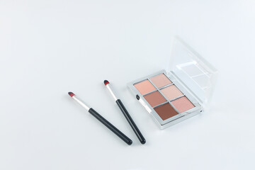 Minimalist flat lay of a nude-toned eyeshadow palette with makeup brushes on a clean white...