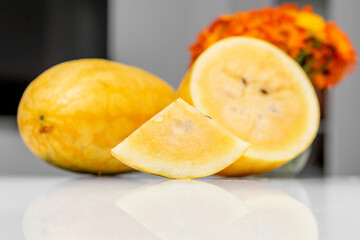 Yellow watermelon slice on reflective white surface with whole fruit in background