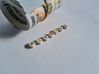 Creative payroll concept with rolled US dollar  and colorful alphabet beads spelling 