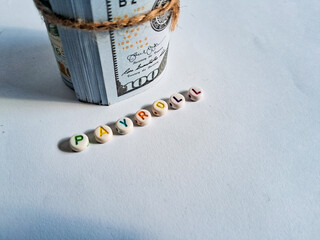 Creative payroll concept with rolled US dollar  and colorful alphabet beads spelling 