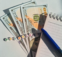 Close-up photo featuring colorful beads spelling “PAYROLL” on US dollar bills, beside a...